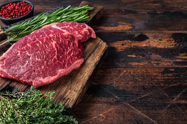 Çiğ Denver et satırıyla kasap tahtasında siyah angus bifteği kesti. Koyu ahşap arka plan. Üst Manzara. Boşluğu kopyala