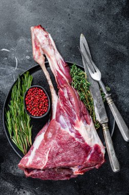 Kemiğin üzerinde çiğ kuzu eti ve otlar. Siyah arka plan. Üst görünüm