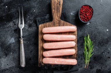 Biberiyeli ahşap bir tahtanın üzerinde taze çiğ tavuk ve hindi eti sosisi. Siyah arka plan. Üst görünüm