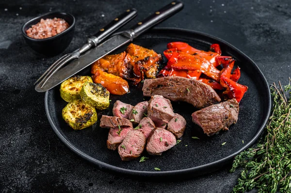 Filet d'agneau ou de chèvre rôti Steak de viande dans une assiette avec légumes grillés. Fond en bois noir. Vue du dessus — Photo