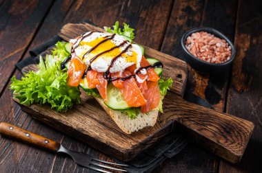 Benedict yumurtalı füme somon sandviçi ve ekmekle avokado. Koyu ahşap arka plan. Üst görünüm