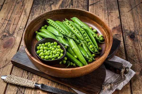 Unpeeled young green pea pods in a wooden plate. wooden background. Top view — Stock Photo, Image