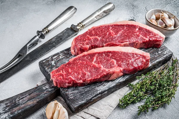 Rauwe rundvlees steaks op houten plank met vleesmes en vork. Witte achtergrond. Bovenaanzicht — Stockfoto