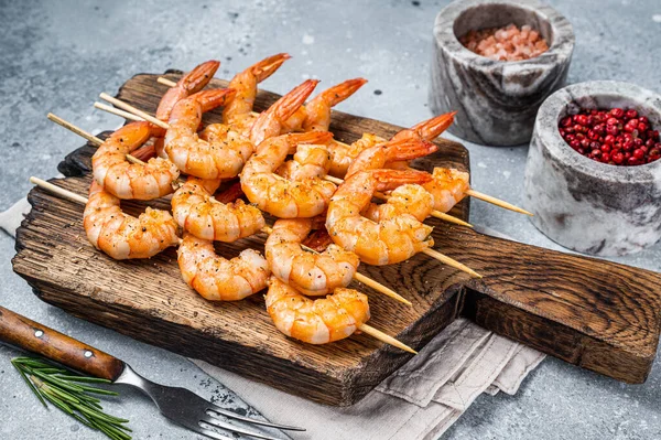 BBQ Camarões assados em espetos em uma tábua de madeira com ervas. Fundo cinzento. Vista superior — Fotografia de Stock