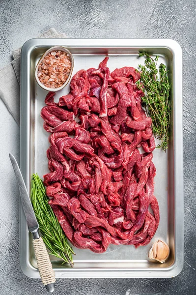 Сирі смужки яловичини в кухонному лотку з розмарином і чебрецем. Білий фон. Вид зверху — стокове фото