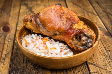 Kırsal ahşap arka planda mayalanmış lahana salatasıyla servis edilen altın çatırdayan kabuklu kızarmış domuz budu.