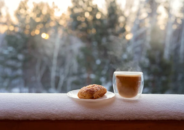 A cup of coffee and cookies stands in the snow. Background of a snowy forest in the sun.