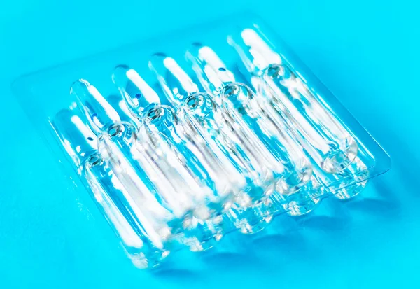 Medical ampoules on the table in transparent packaging on a blue background. Medical glass ampoules close up.