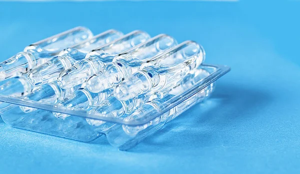 Medical ampoules on the table in transparent packaging on a blue background. Medical glass ampoules close up.