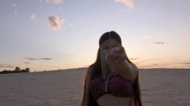 Doğu tarzı takıları olan güzel bir kadın gün batımında doğuda göbek dansı yapıyor. Orta uzunlukta..