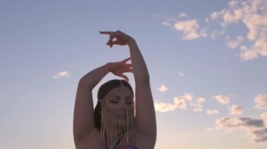 Doğu tarzı takıları olan güzel bir kadın gün batımında doğuda göbek dansı yapıyor. Yakın çekim..