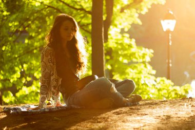 Güzel kız ağaçların yanındaki parkta oturur ve gitar çalar.