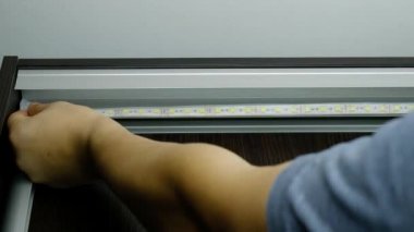 Usta LED 'i tutkallıyor ve aydınlatma için dolabı soyuyor. diyot ışıklandırma bandı kurulumu