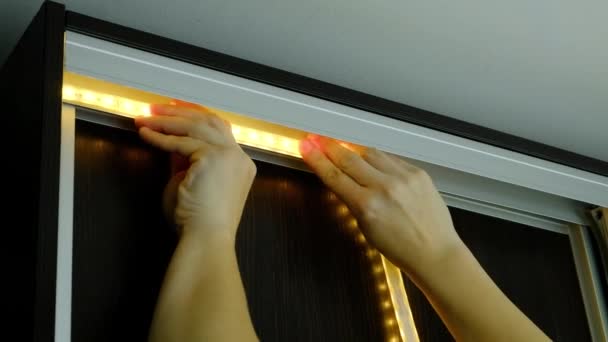 Майстер клеює світлодіодну смугу на металевий профіль кабінету — стокове відео