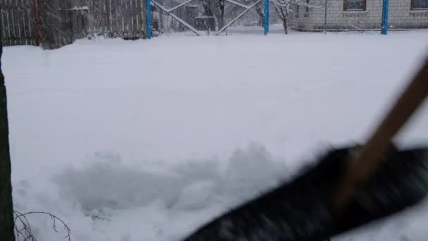 Um homem limpa um caminho da neve com uma pá de neve durante uma queda de neve close-up — Vídeo de Stock