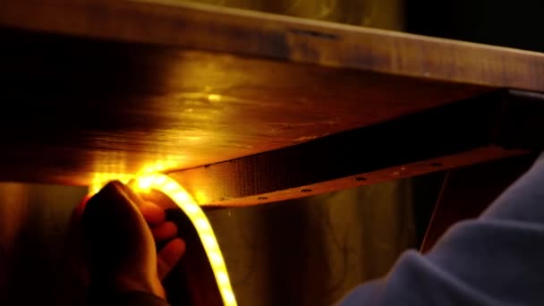나무로 된 탁자 밑에 LED 띠를 설치하는 모습, 장식용 조명 — 비디오