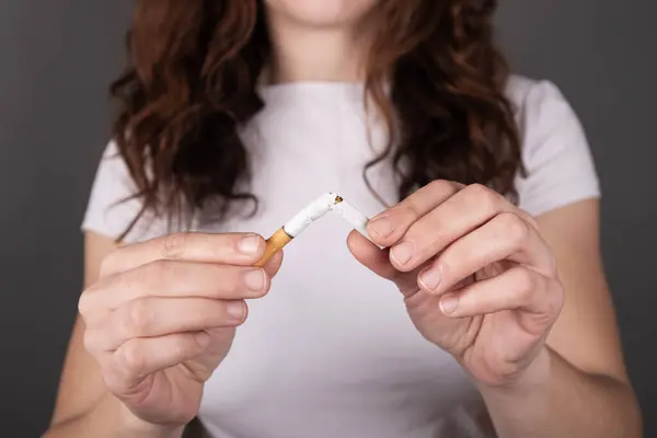 broken cigarette in female hands, stop smoking sign.