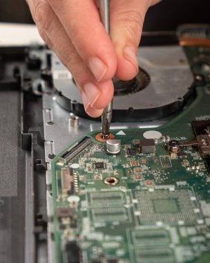 Bilgisayar bakımı, servis merkezinin ustası ana kartın vidalarını tornavidayla açıyor.