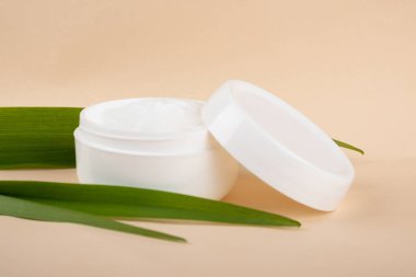 cosmetic cream and green leaf on beige background. skin care.