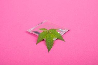 Pembe arka planda prezervatif ve marihuana yaprağı..