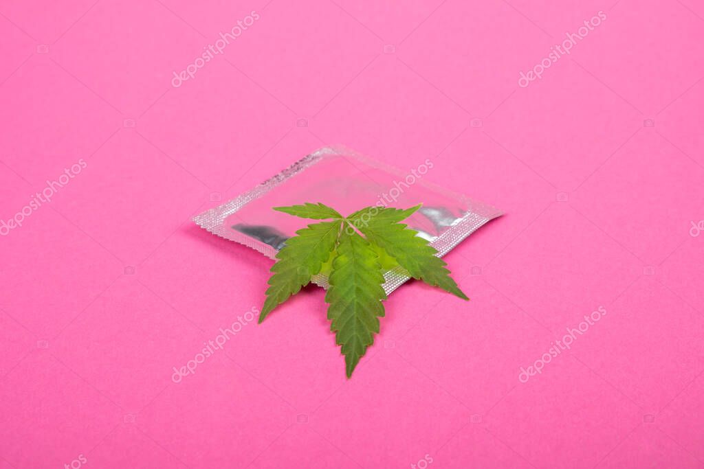 Condom and marijuana leaf on a pink background close-up.