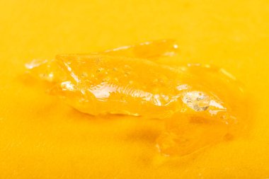 golden dab concentrate of cannabis wax close up on yellow background, marijuana resin