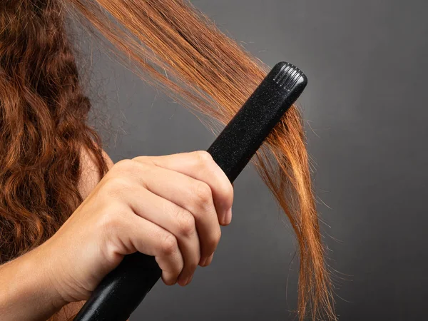 Flicka slätar lockigt hår med en hår plattång, locktång — Stockfoto