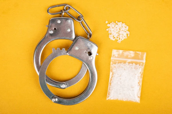 Хрустальные наркотики и наручники на желтом фоне, торговля белым порошком — стоковое фото