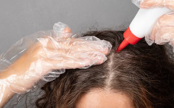 Een vrouw brengt kleurstof aan op de wortels van haar haar verft grijs grijs haar — Stockfoto