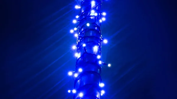 Un pilar envuelto en un fondo azul de guirnaldas navideñas — Foto de Stock