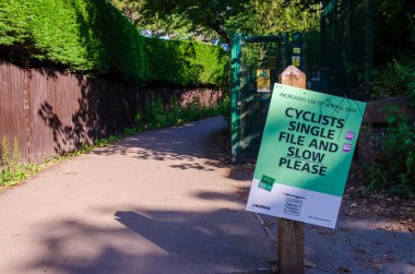 Caldy, UK: 23 Haziran 2020: The Wirral Way bisiklet pisti ve patikasının girişindeki bir işaret Corona Virüs salgını sırasında artan kullanım nedeniyle bisikletçilerin yavaş ve tek sıra halinde gitmesi gerektiği uyarısında bulundu