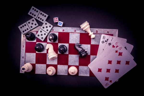 Various board games and figurines over checkers board — Stock Photo, Image