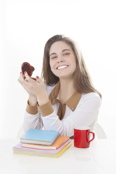 Linda chica morena con taza de café y libros de color en estudio haciendo maquillaje — Foto de Stock