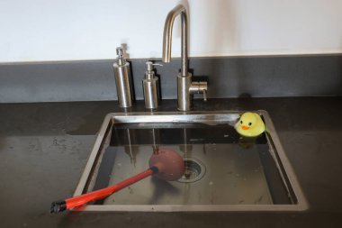 Mutfak lavabosu taşmış, kanalizasyon tıkanmış. Pompa (güç bardağı) ve sarı plastik ördek lavaboda. Tesisat sorunları.