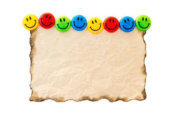 Burned old paper with colorful smile magnet on white background.