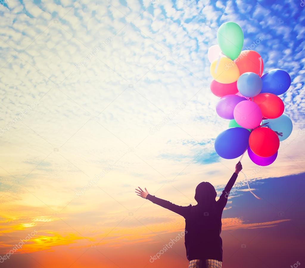 girl holding bunch of air balloons at sunset sky