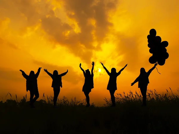 Silhouetted girl holding bunch of air balloons runing at sunset — Stock Photo, Image