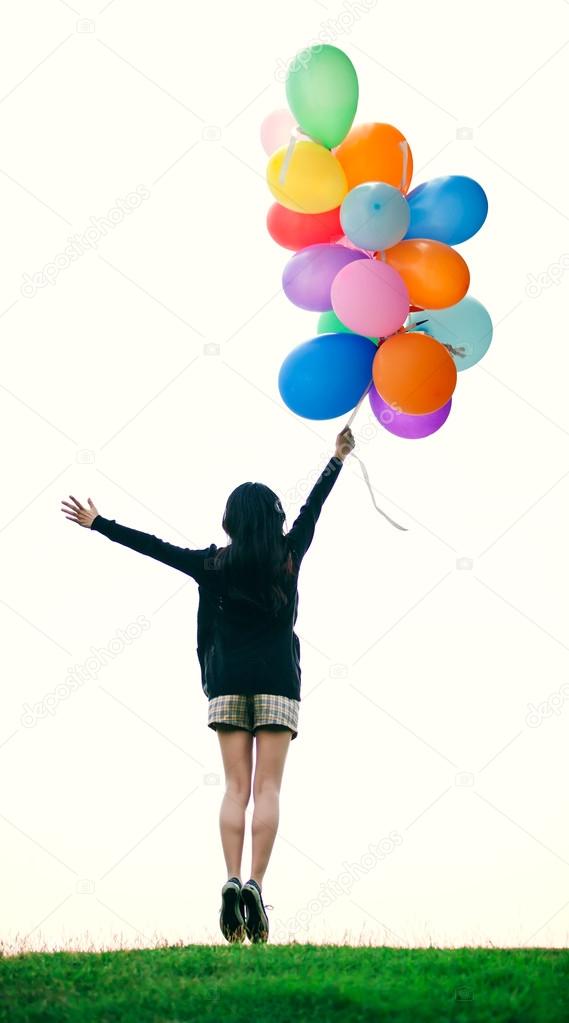 Happy girl holding bunch of colorful air balloons jumping in gra