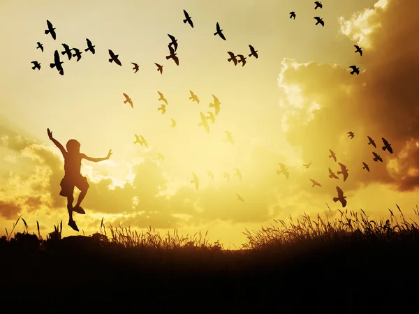 Criança feliz pulando com pássaros no céu do por do sol . — Fotografia de Stock