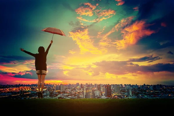 Menina feliz com guarda-chuva vendo pôr do sol sobre a cidade . — Fotografia de Stock