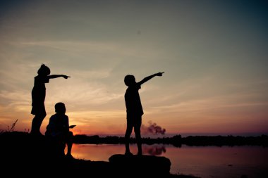 Siluet çocuklar gün batımında mutlu vakit geçiriyorlar. 