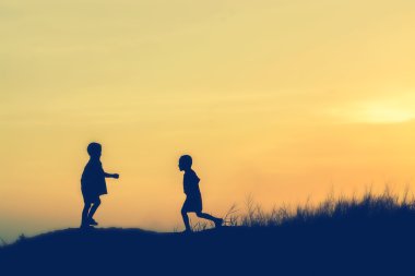 Siluet çocuklar gün batımında mutlu vakit geçiriyorlar. 