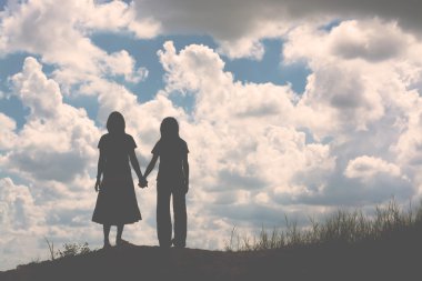 Birbirine bakan iki kızın silueti el ele tutuşuyor.