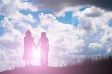 Birbirine bakan iki kızın silueti el ele tutuşuyor.