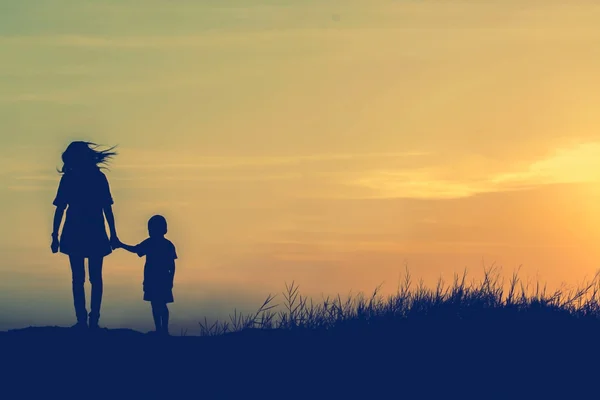 Mother encouraged her son outdoors at sunset, silhouette concept