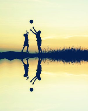 günbatımı su yansıması ile futbol oynayan çocuklar. silhouett
