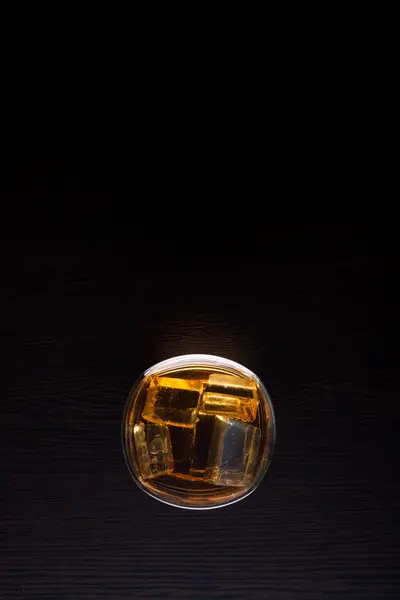 Bovenaanzicht van whisky in glas met ijs op zwarte achtergrond — Stockfoto