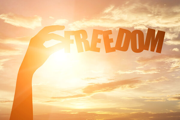 silhouette of a hand holding "freedom" paper text