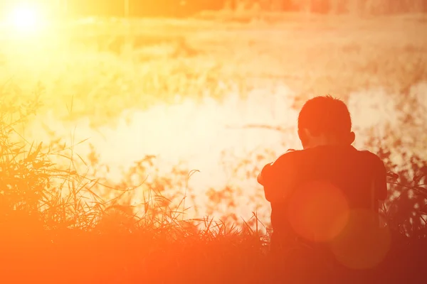 Triest eenzame jongen zitten op gras weg op zoek naar rivier. — Stockfoto