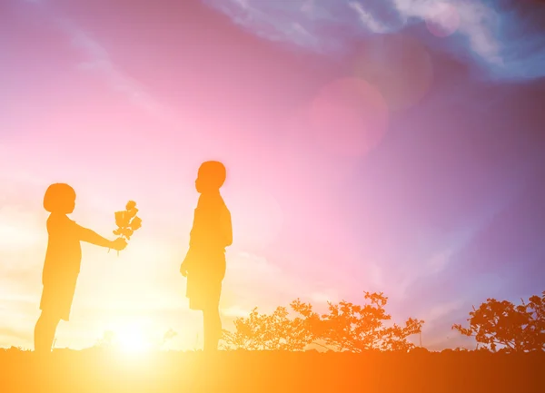 Niña dar una flor a niño pequeño, concepto de silueta — Foto de Stock